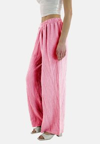 Roze, wijde katoenbroek met een gekreukelde structuur en elastische tailleband. Gecombineerd met witte haksandalen, zijkant zichtbaar.