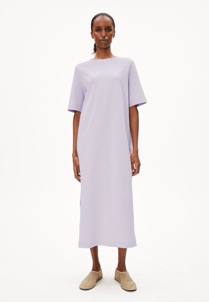 Robe maxi à manches courtes lavande avec une coupe droite, des fentes latérales et un tissu doux. Associée à des chaussures beiges à enfiler. Fond blanc.