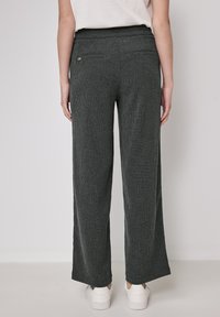 Mörkgrå, texturerade vida byxor med hög midja, två bakfickor och avslappnad passform, som är tillsammans med vita sneakers.