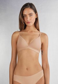 Naadloze draadloze bh in huidskleur met een driehoekig ontwerp, dunne bandjes en een gladde textuur. Gekocht met een low-rise slip.