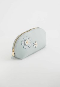 Funda con cremallera de color azul claro hecha de material suave, con dos apliques decorativos de flores en blanco y azul pálido, y hardware dorado en la cremallera.
