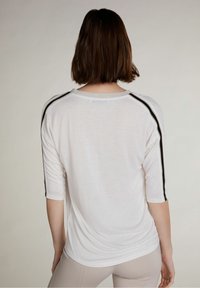Camicia leggera bianca con maniche a tre quarti, scollo grigio, strisce laterali nere e texture morbida e liscia.