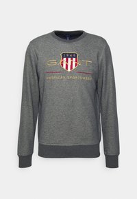 Sudadera gris de manga larga con cuello redondo y puños acanalados. Logo bordado en forma de escudo con acentos en rojo y dorado. Tejido suave.