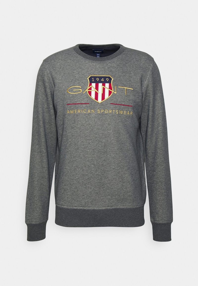 Sudadera gris de manga larga con cuello redondo y puños acanalados. Logo bordado en forma de escudo con acentos en rojo y dorado. Tejido suave.