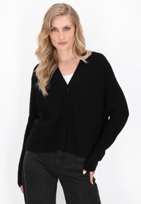Cardigan nero a coste con scollo a V e chiusura a un bottono. Presenta maniche lunghe e vestibilità comoda, abbinato a jeans neri.