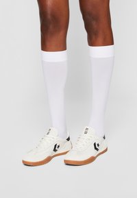 White sneakers with black accents, textured fabric, and rubber soles; paired with knee-high, fitted white socks.