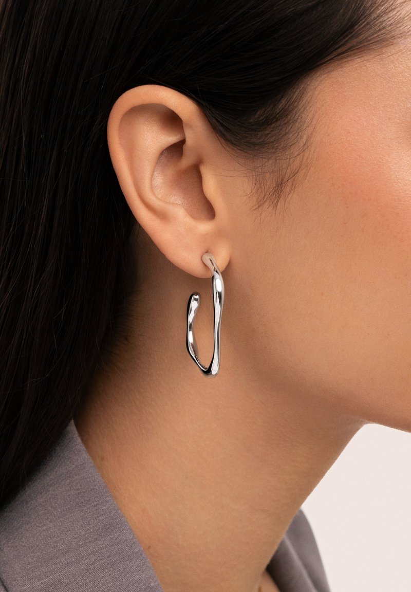 Pendientes de aro de plata con una forma fluida irregular, con un acabado pulido y un diseño de aro delgado.