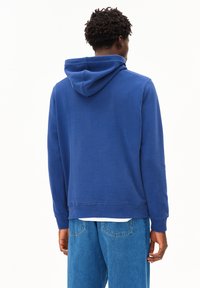 Blaues Fleece-Hoodie mit verstellbarem Kapuzenzug, gerippten Bündchen und Saum. Getragen mit hellblauen Jeans, die eine lässige Passform zeigen.