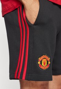 Calções atléticos pretos com três riscas vermelhas nas laterais e um logótipo bordado do Manchester United na perna esquerda.