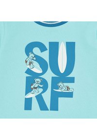 Camiseta de color azul claro con un cuello acanalado, que presenta un gráfico de tres osos de peluche surfeando y el texto "SURF" en letras azules en negrita.