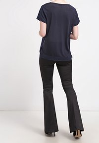 Marinblus med kort ärm och avslappnad passform, i kombination med svarta utsvängda byxor. Slät tyg med sidofågel och en rundad fåll.