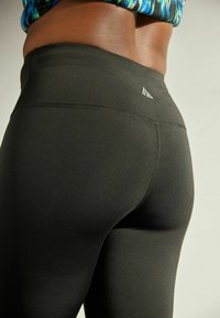 Zwarte sportleggings van een gladde, rekbare stof. Kenmerkt zich door een hoge tailleband en een klein logoaccent op de achterkant.