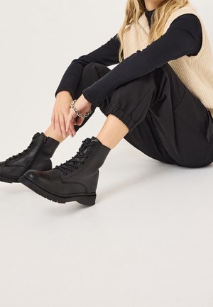 Sorte snørebånd ankelstøvler med en glat læderoverflade, rund tå og tekstureret gummisål. Lynlåslukning på siden.