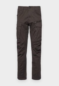 Nákladní kalhoty v tmavě hnědé látce s několika kapsami, zipovou kapsou na stehně a rovnými nohavicemi. Jsou viditelné zesílené švy.