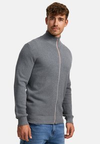 Grå hettegenser med glidelås, med teksturert strikkemønster, høy krage og kontrasterende glidelås. Tettsittende design med ribbestrikkede mansjetter og kant.