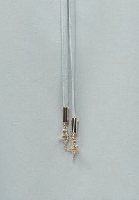 Hellblauer, strukturierter Stoff mit zwei dünnen Bändern, die in goldfarbenem Metall enden und die Form von Muscheln haben. Glatte Oberfläche und langlebiges Material.