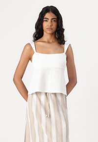 Top en lin blanc à encolure carrée et bretelles larges, associé à une jupe en beige rayée avec cordon de serrage. Texture douce, tissu léger.