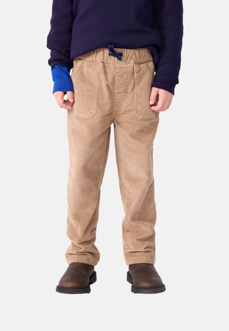 Pantaloni in corduroy beige con una cintura elastica, due tasche frontali e una vestibilità ampia. Abbinati a stivaletti marroni e una maglietta blu navy.