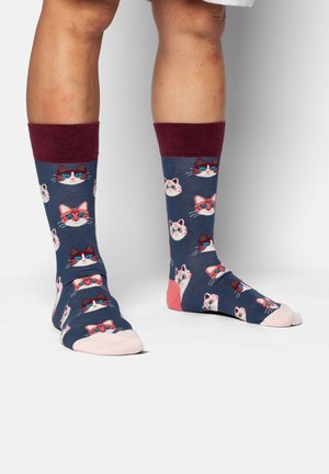 Benen met kniekousen in marineblauw met wijnrode manchetten, versierd met verschillende kleurrijke kattengezichten, gecombineerd met lichtroze tenen en hielen.