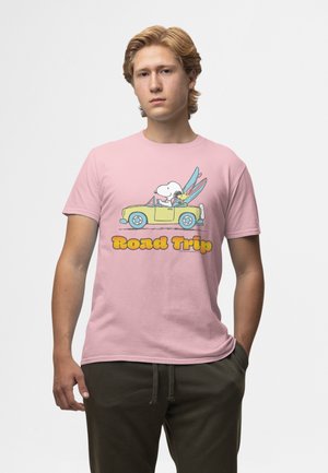 Giovane uomo che indossa una camicia rosa con Snoopy e Woodstock che guidano una decappottabile gialla e la scritta "Road Trip".