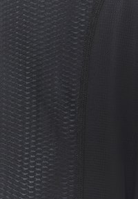Black athletic top made of textured fabric, featuring a wavy pattern and smooth accents. It has a fitted design with a seam detail.