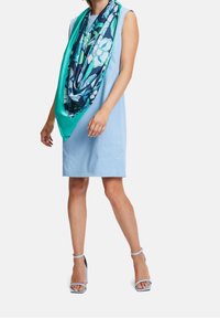 Jasnoniebieska sukienka bez rękawów w połączeniu z dużym szalem w kwiatowy wzór w odcieniach niebieskiego i zielonego. Dopełniają ją pasujące, niebieskie sandały na kostkę.