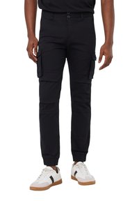 Czarne spodnie cargo z elastycznymi mankietami, z wieloma bocznymi kieszeniami i dopasowanym krojem. W połączeniu z białymi trampkami z czarnymi akcentami.