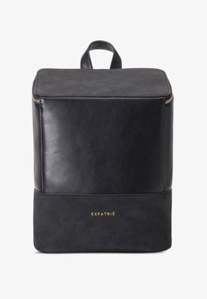 Schwarzer Leder-Rucksack mit quadratischer Form, oberem Griff, goldenem Reißverschluss und goldenem "EXPATRIÉ" Logo auf dem unteren Frontpaneel.