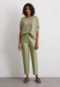 Light green oversized sweater paired with light green trousers, featuring a relaxed fit. Brown sandals with a gold buckle detail.