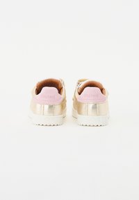 Złote sneakersy o teksturowanym wykończeniu, z różowym językiem, białą gumową podeszwą i przeszyciami.