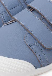 Hellblaue synthetische Schuhe mit zwei Klettverschlüssen, strukturierten Oberflächen, weißer Gummisohle und kontrastierendem braunem Nähte.