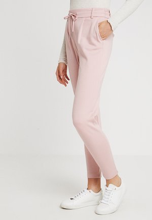 Pantaloni della tuta rosa a sigaretta con vita regolabile con coulisse, tasche laterali e polsini elasticizzati, abbinati a scarpe da ginnastica bianche. Tessuto dalla texture liscia.