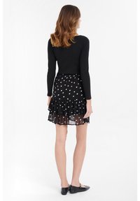 Crni longsleeve top uparen s prozirnom crnom suknjom koja ima bijele točkice i volanasti rub. Nosite s crnim balerinkama.