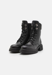 Bottines en cuir noir avec un laçage à l'avant, matériel argenté, col rembourré et semelle chunky noire. Texture lisse et design robuste.