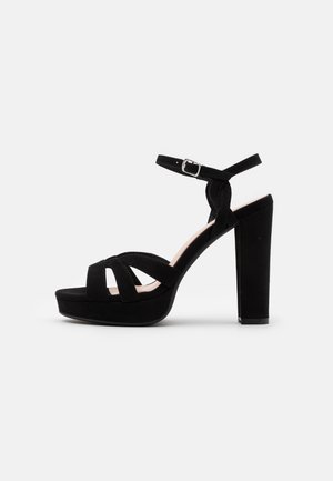 Sort højhælet sandal med en platformsål, tre frontremme og en ankelrem med en sølv spænde.