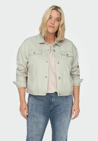 Chaqueta de mezclilla gris claro con mangas largas, cierre de botones en la parte delantera y dos bolsillos en el pecho. Destaca por su corte relajado y los detalles de las mangas enrolladas.