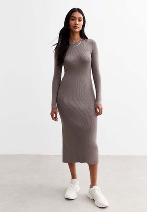Robe en tricot côtelé couleur brun clair, à manches longues, silhouette ajustée, atteignant le milieu du mollet, associée à des baskets blanches de sport.