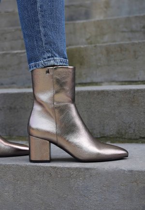 Botín metálico plateado hasta el tobillo con punta afilada y tacón grueso. Hecho de cuero suave, presenta costuras sutiles y un detalle de logotipo.