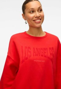 Roter Sweatshirt mit Rundhalsausschnitt, das mit fett gedrucktem "LOS ANGELES" und "HOLLYWOOD BLVD" in kleinerer Schrift versehen ist. Hergestellt aus weichem Stoff mit lockerer Passform.