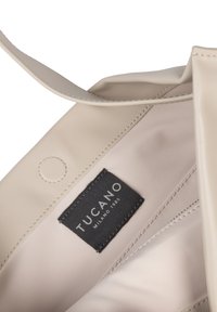 Interieur van een beige leren tas met een zwart stoffen label waarin "TUCANO MILANO 1985" is gestikt.