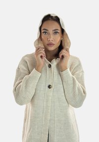 Cardigan con cappuccio beige chiaro in tessuto lavorato a maglia, chiusura anteriore con bottoni e polsini a costine, caratterizzato da una vestibilità comoda e un aspetto accogliente.