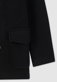 Manica di un cappotto di lana nera con una grande tasca a soffietto rettangolare con bordi arrotondati su uno sfondo semplice.