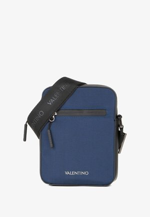 Sac en tissu bleu marine avec accents noirs, forme rectangulaire, sangle ajustable, poche zippée à l'avant et détail du logo sur la sangle.