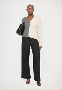 Kootud kahes toonis kardigan helesinises ja kreemis, millel on kaablimuster. Sobitatud mustade peenekoeliste laiade pükstega ja tekstureeritud musta kotiga.