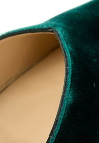 Gros plan de l'intérieur d'une chaussure en velours vert foncé montrant une semelle beige et des coutures détaillées le long du bord.