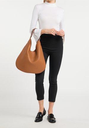 Bruine leren hobo tas met een slungelige vorm, een voorkantvak en een chunky kettingriem. Gecombineerd met zwarte strakke broeken en een witte top.