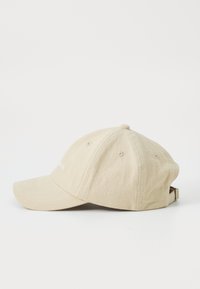 Gorra de béisbol beige hecha de tela texturizada, con visera curva, agujeros de ventilación y una correa ajustable en la parte posterior.