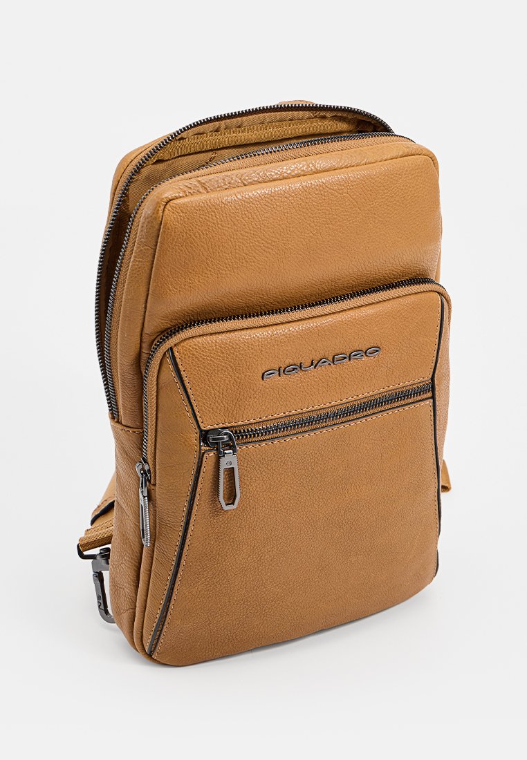 Zaino in pelle tan con finitura testurizzata, dotato di tasca frontale con zip, chiusura superiore con zip e cuciture in contrasto. Logo del marchio sulla parte anteriore.