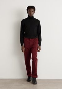 Un pull à col roulé noir, un pantalon tapered bordeaux et des baskets noires. Des tissus lisses avec une silhouette ajustée et des caractéristiques de design minimalistes.