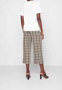 Witte kortemouwen top met gerimpelde manchetten, gecombineerd met cropped geruite broeken in bruine, beige en zwarte tinten. Zwarte block-heeled sandalen.